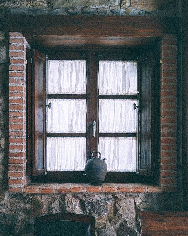 Ventana rústica de piedra y ladrillo con cortinas y una jarra de barro