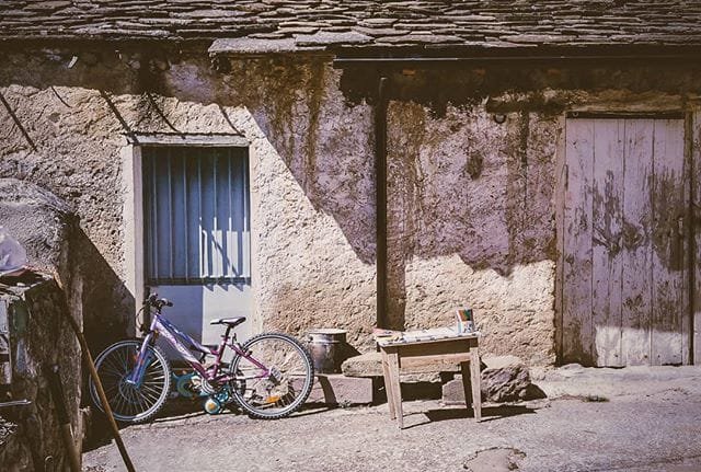 Fachada de una casa rústica de piedra con una bicicleta apoyada y puerta azul