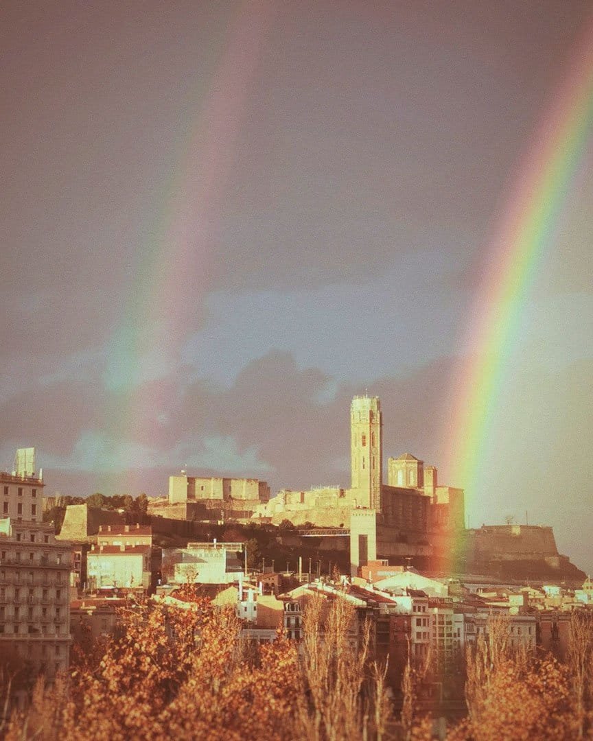 Doble arco iris sobre un pueblo con una torre, al atardecer